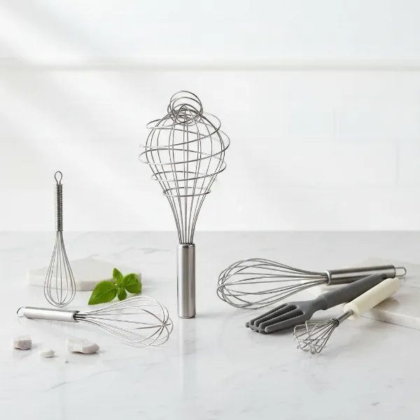A curated selection of various kitchen whisks laid out on a clean kitchen counter, showcasing different types and materials with good lighting.